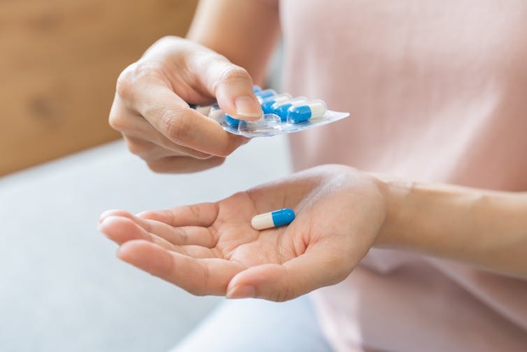 A woman places a pill from a blister pack of medication into her hand.